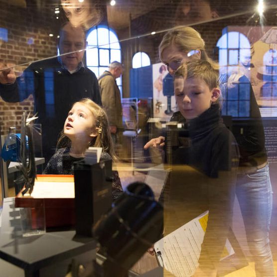 Familie und Museumsleitung an einer Vitrine mit Ausstellungsstücken im Museum zur Vorgeschichte des Films in der Camera Obscura Mülheim 