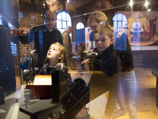 Familie und Museumsleitung an einer Vitrine mit Ausstellungsstücken im Museum zur Vorgeschichte des Films in der Camera Obscura Mülheim 