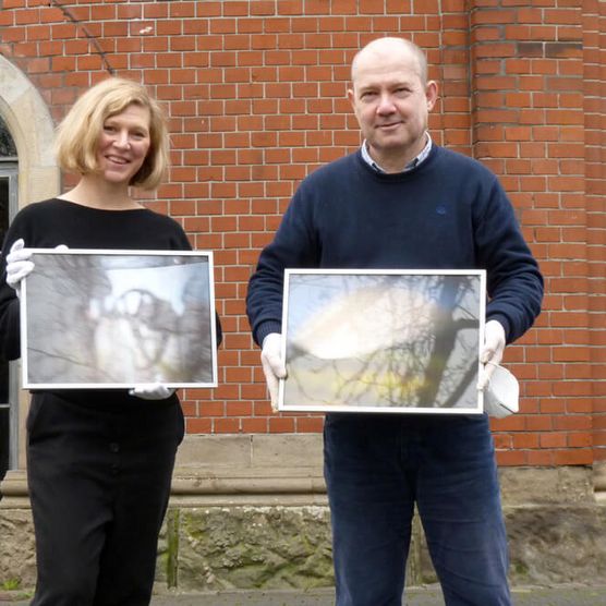 Vanessa Leissring, Lehrerin der Werner von Siemes-Schule, mit Dr. Jörg Schmitz und Bildern des Schulprojekts „CameraObscura-BlackBox”, die 2022 in der Camera Obscura ausgestellt wurden 