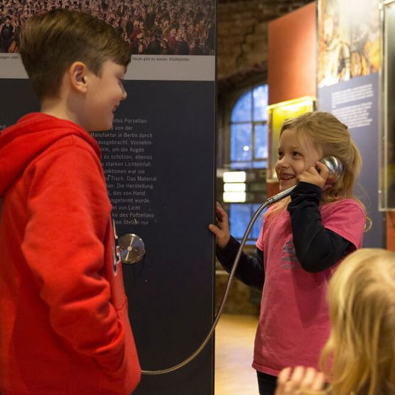 Kinder an einem Hörer mit Audioinfos im Museum zur Vorgeschichte des Films in der Camera Obscura Mülheim